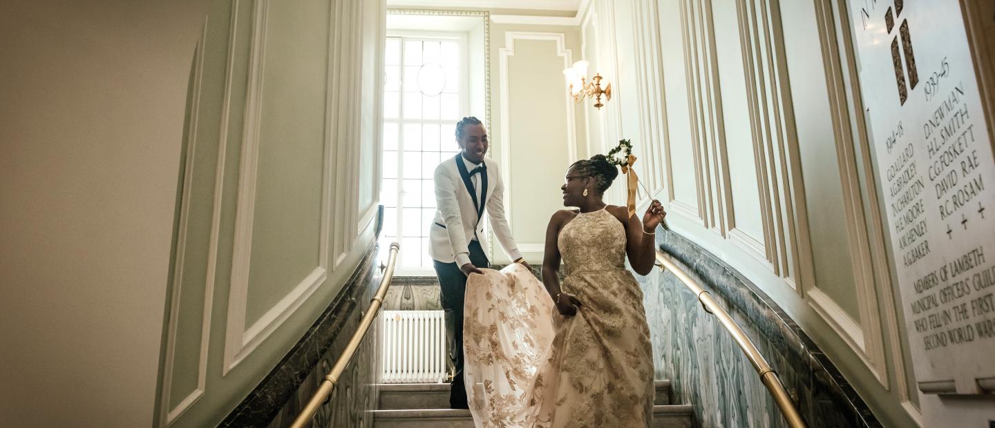 Couple walk down the marble stairs of the Circular Hall with the groom holding the train of the bride's wedding gown 