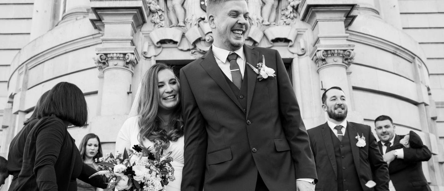 Black & White image of newlyweds leaving Lambeth Town Hall with friends and family behind 