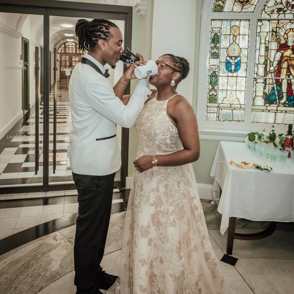 Couple share a drink from "Bride & Groom" cups during a drinks reception