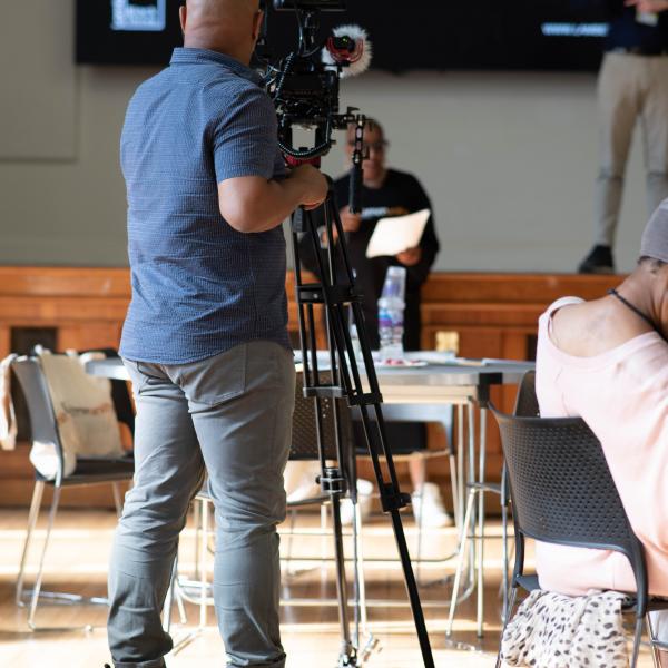 Image of man holding camera on tripod shooting a community event on stage in Lambeth Town Hall