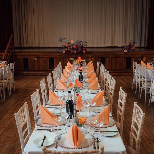 long tables dressed for wedding breakfast with cream chairs and orange napkins