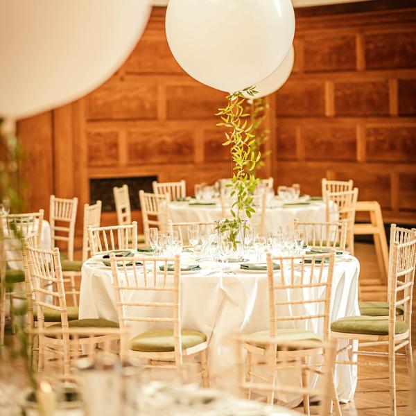 venue set up for wedding, with white linen, white balloons and wooden chairs with green pad