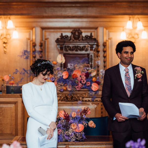 Couple during ceremony with backdrop of orange and purple flowers 