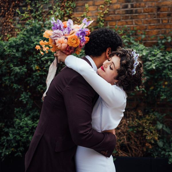 Couple hug on wedding day with orange and purple floral bouquet